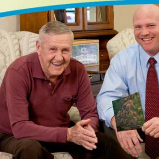Two men smiling while sitting indoors, one holding a card.