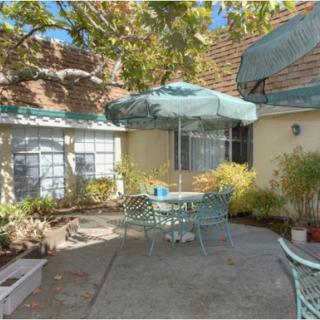 A tranquil outdoor patio perfect for relaxation, featuring a table with an umbrella surrounded by lush greenery.