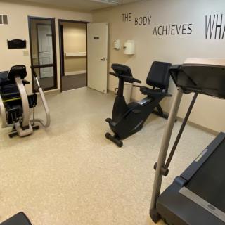A small fitness room with exercise equipment including a treadmill and stationary bike, featuring a motivational quote on the wall.
