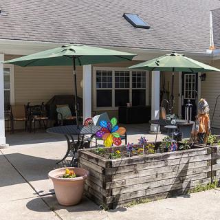 A cozy patio setup with shaded seating, vibrant flowers, and a decorative pinwheel.
