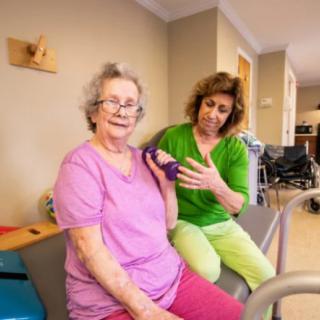 A healthcare professional assists an elderly woman during a physical therapy session.