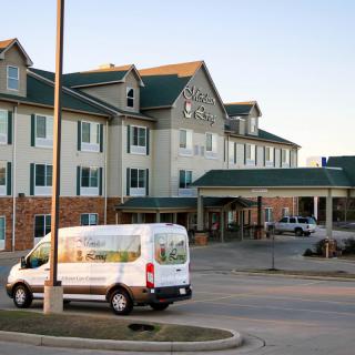 A hotel entrance with a shuttle van parked in the lot.