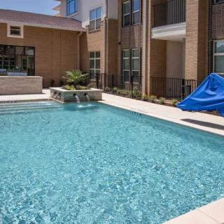 A modern apartment complex featuring an outdoor swimming pool on a sunny day.