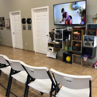 A cozy waiting area featuring chairs, a television displaying children at play, and shelves with toys.