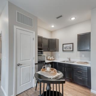 A modern and compact kitchen in an apartment setting with dark cabinets and a small dining table.