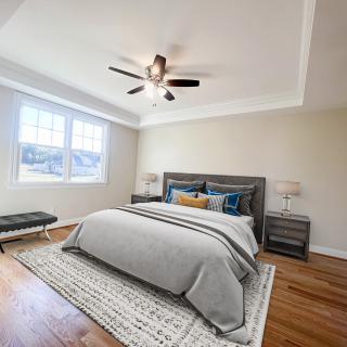 A modern bedroom featuring a large bed with neutral bedding, a ceiling fan, and ample natural light from the window.