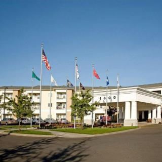 A hotel building with flags displayed at the entrance and a parking area in front.
