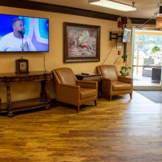 A cozy waiting area with comfortable chairs and a television, featuring warm wooden flooring.