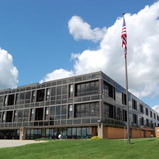 A modern architectural building with large windows and an American flag waving in front.