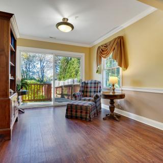 A cozy living room with a plaid chair, wooden flooring, and large windows overlooking greenery.
