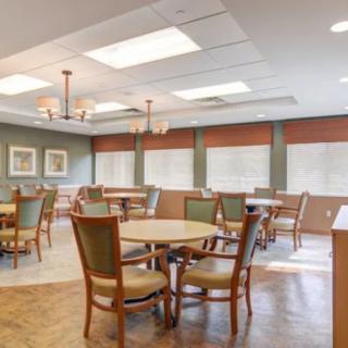 A spacious and well-lit dining area with multiple tables and chairs, featuring large windows and decorative lighting.
