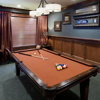 A stylish billiard room featuring a pool table with cues, surrounded by wood paneling and warm lighting.