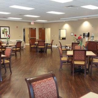 An interior view of a dining room with chairs and tables arranged neatly, featuring wooden flooring and bright lighting.