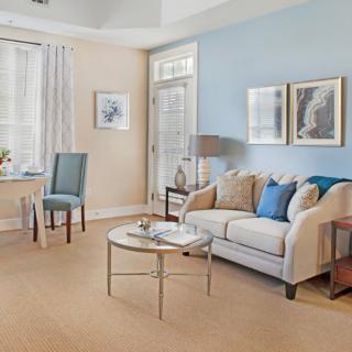 A cozy living room with blue and beige tones, featuring a comfortable sofa, decorative pillows, a round coffee table, and framed artwork on the walls.