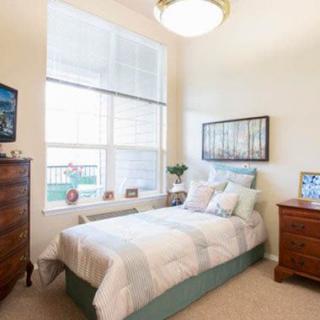 A cozy bedroom with a large window, featuring a single bed, wooden furniture, and soft lighting.