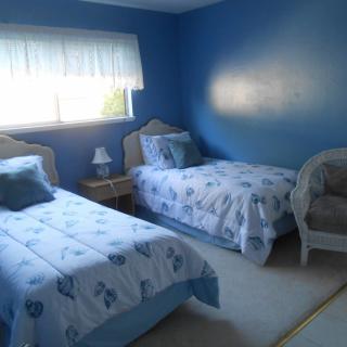 A cozy bedroom with two twin beds, light blue walls, and a window bringing in sunlight.