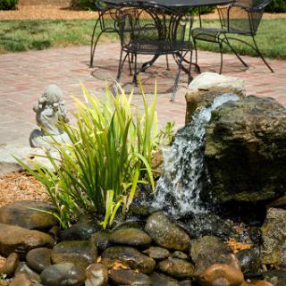 A serene garden scene featuring a small fountain surrounded by rocks and lush greenery, perfect for relaxation.