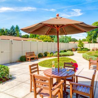 A sunny patio with wooden furniture and an umbrella, surrounded by a landscaped garden.
