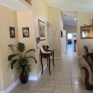 A cozy living space with a tiled hallway, decorated with plants, artwork, and furniture.