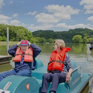 An elderly couple enjoying a leisurely paddle boat ride on a scenic lake.