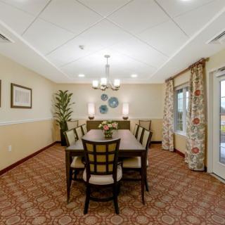 A well-decorated dining room with a central table, surrounded by chairs, featuring elegant lighting and tasteful decor.