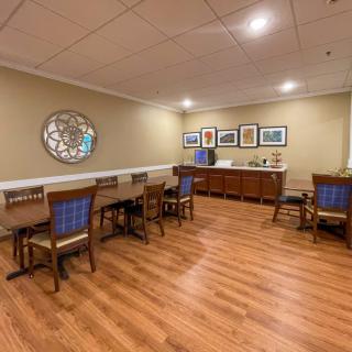 A cozy dining area with neatly arranged tables and chairs, featuring wall art and a hardwood floor.