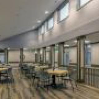 A spacious dining area with tables and chairs, featuring large windows letting in natural light.