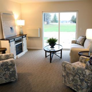A cozy living room with a sofa, two chairs, a glass coffee table, and a fireplace.