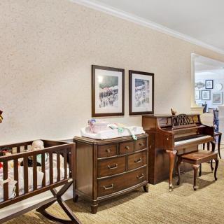 A cozy nursery featuring a crib, dresser, and piano with framed artwork on the wall.