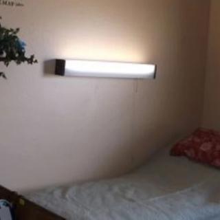 A minimalist bedroom with a wall-mounted light above the bed.