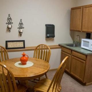 A small kitchen area with a round wooden table and chairs, featuring a microwave on the countertop and decorative items on the walls.