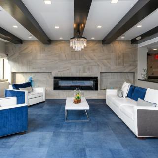 A modern living room with blue carpeting, white furniture, and a sleek fireplace.