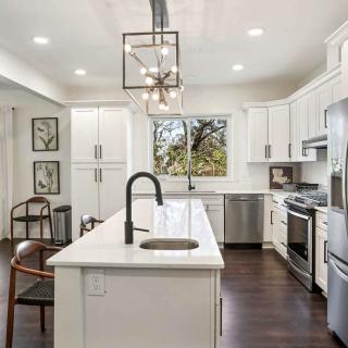 A modern kitchen featuring white cabinets, an island, stainless steel appliances, and pendant lighting over a hardwood floor.