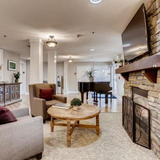 A cozy living room with a fireplace, TV, and piano, featuring modern decor and comfortable seating.