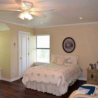 A cozy bedroom with a neatly made bed, ceiling fan, and natural light from a window.