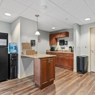 A modern office kitchen featuring a refrigerator, water cooler, and wooden cabinetry.