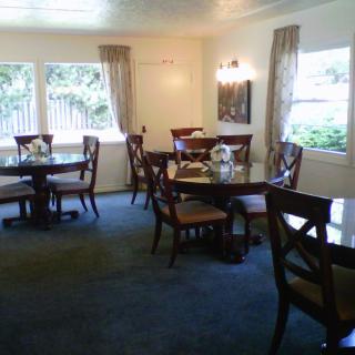 An elegant dining room with multiple tables and chairs, large windows with curtains, and a blue carpet.