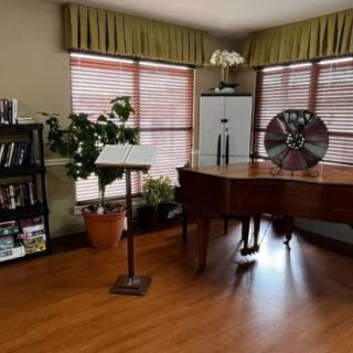 A cozy music room featuring a grand piano, bookshelf, and decorative plants.