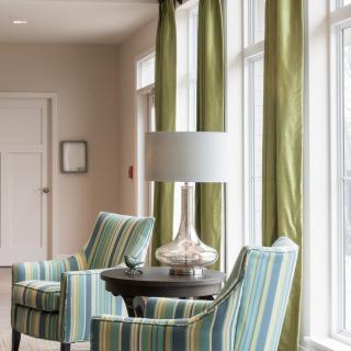 A cozy living room corner with striped chairs, a lamp, and green curtains.