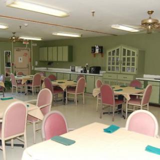 A communal dining area with pink chairs and tables, featuring a kitchen in the background.