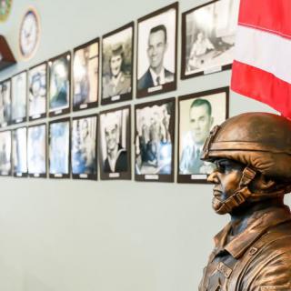 A military-themed display featuring a soldier's statue and wall of portraits with an American flag.