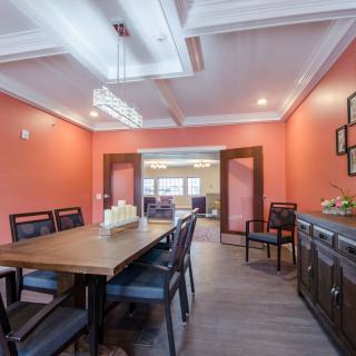 A modern dining room with orange walls, a wooden table surrounded by chairs, and elegant ceiling lighting.
