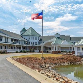 A picturesque view of a building with an American flag in front, surrounded by landscaped grounds and a serene water feature.