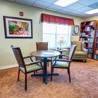 A cozy reading room with a table, chairs, and a bookshelf by the window.