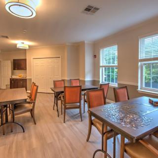 A well-lit dining area with multiple tables and chairs, adjacent to a kitchen space.