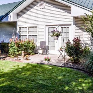 A cozy backyard with a well-maintained lawn, patio seating, and vibrant garden plants in front of a charming house.