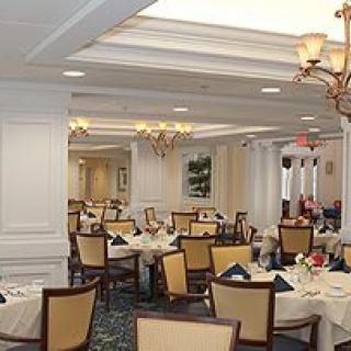 An elegant restaurant dining room with neatly arranged tables and chairs, featuring chandeliers and tasteful decor.