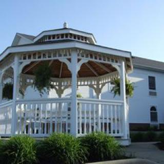 A charming white gazebo in front of a building, surrounded by greenery under a clear blue sky.