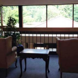 A cozy seating area with two chairs and a table by large windows overlooking greenery.