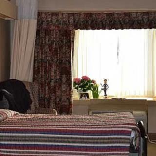 A cozy bedroom featuring a neatly made bed and a window with floral curtains, allowing natural light to brighten the room.